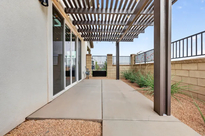 Concrete patio with a wood-finish pergola, stucco exterior, and black metal fencing