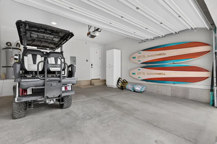 Concrete flooring, white painted walls, overhead garage door, built-in white cabinetry, interior access door