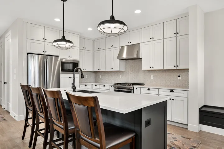 Kitchen featuring white shaker cabinetry, stainless steel appliances, a center island with a white countertop, wood-finish flooring, and pendant lighting