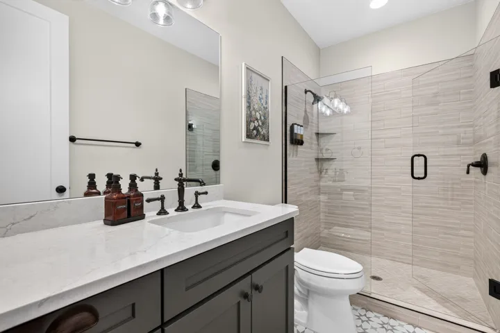 Vanity with a white countertop and dark cabinetry, contemporary shower with clear glass enclosure, tiled shower walls, and patterned floor tile