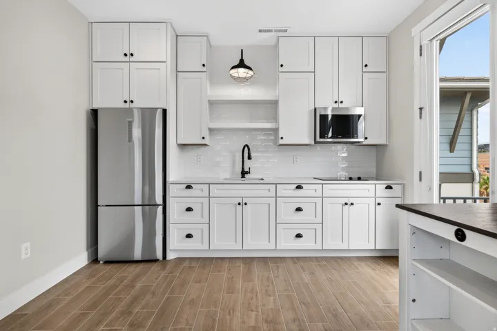 Kitchenette featuring white shaker cabinetry, stainless steel appliances, wood-finish flooring, a white subway tile backsplash, and a modern pendant light fixture