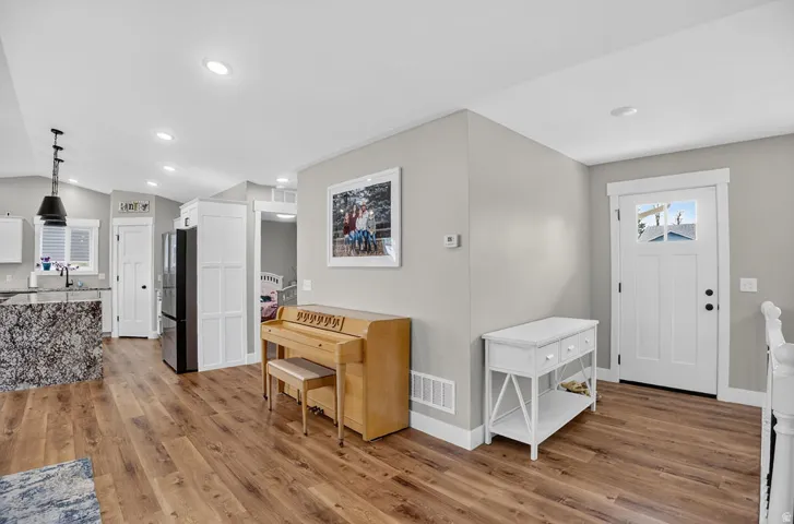 Wood-finish flooring throughout, recessed ceiling lighting, kitchen island with stone countertop, white paneled entry door with glass insert, and white baseboards