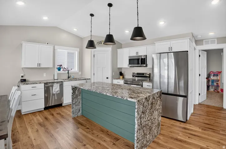 Gourmet kitchen featuring white cabinetry, stainless steel appliances, wood-finish flooring, a center island with a waterfall countertop, and pendant lighting