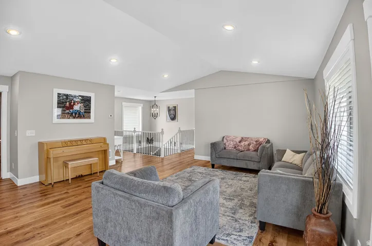 Wood-finish flooring throughout, vaulted ceiling, recessed lighting, white window blinds, and white painted railings