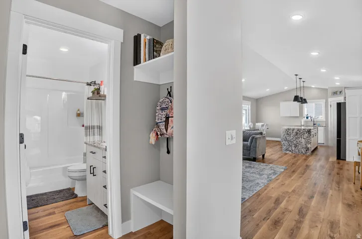 Wood-finish flooring throughout, white shaker-style cabinetry with dark hardware, recessed lighting, and a built-in entry bench with shelving
