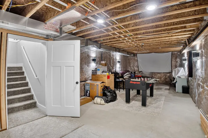Finished lower level with exposed joists, recessed lighting, and wall-mounted sconces