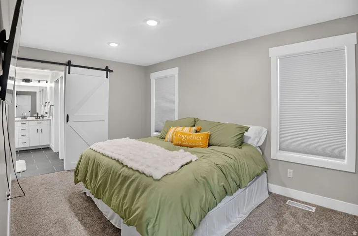 Recessed ceiling lighting, barn door entry, carpet flooring, window with cellular blinds, and a vanity with a countertop and cabinets