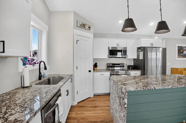 Stainless steel appliances, white cabinetry with black hardware, wood-finish flooring, island with shiplap detail, and patterned countertops