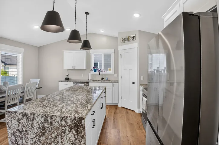 Kitchen featuring a large central island with a stone countertop, white cabinetry, stainless steel refrigerator, and wood-finish flooring