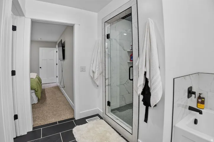 Walk-in shower with clear glass enclosure, black-framed shower door, and marble-look tile surround