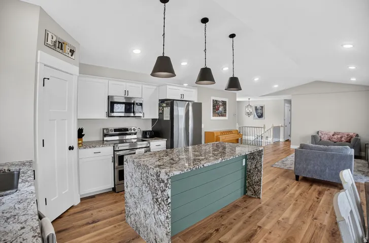Modern kitchen with white cabinetry, stainless steel appliances, a large island featuring a shiplap base and granite countertop, and wood-finish flooring