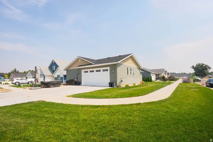 Single-story residence featuring light gray siding with white trim, a dark shingled roof, a two-car garage, and a concrete driveway