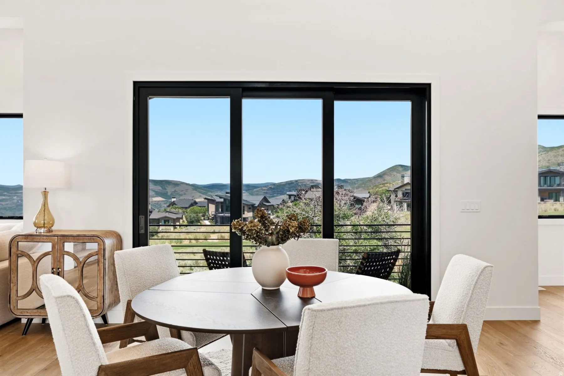 Expansive floor-to-ceiling sliding glass doors, white walls, light wood-finish flooring, and a mountain backdrop
