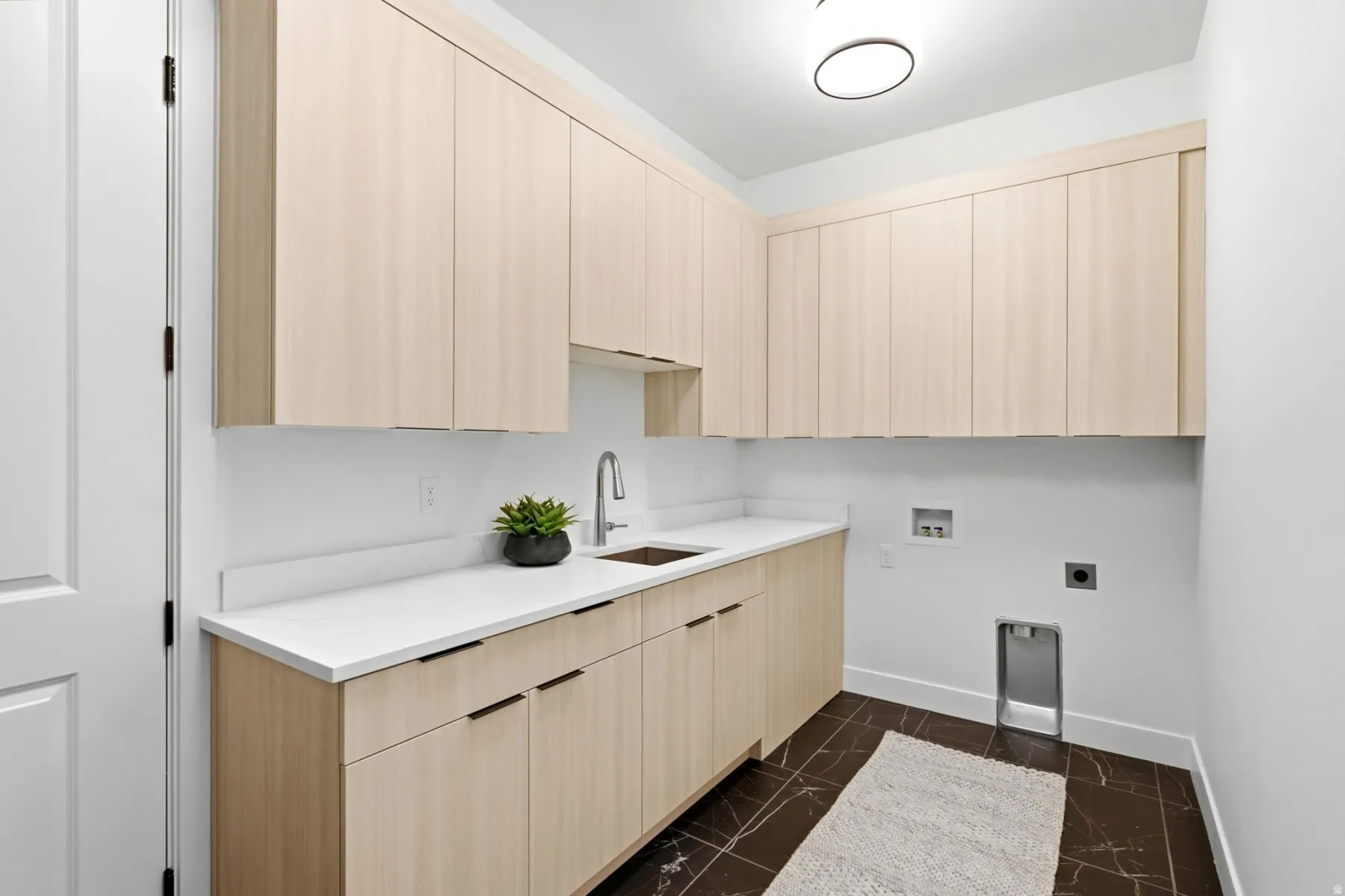 Light wood-finish cabinetry, white countertops, built-in sink with gooseneck faucet, and dark tile flooring