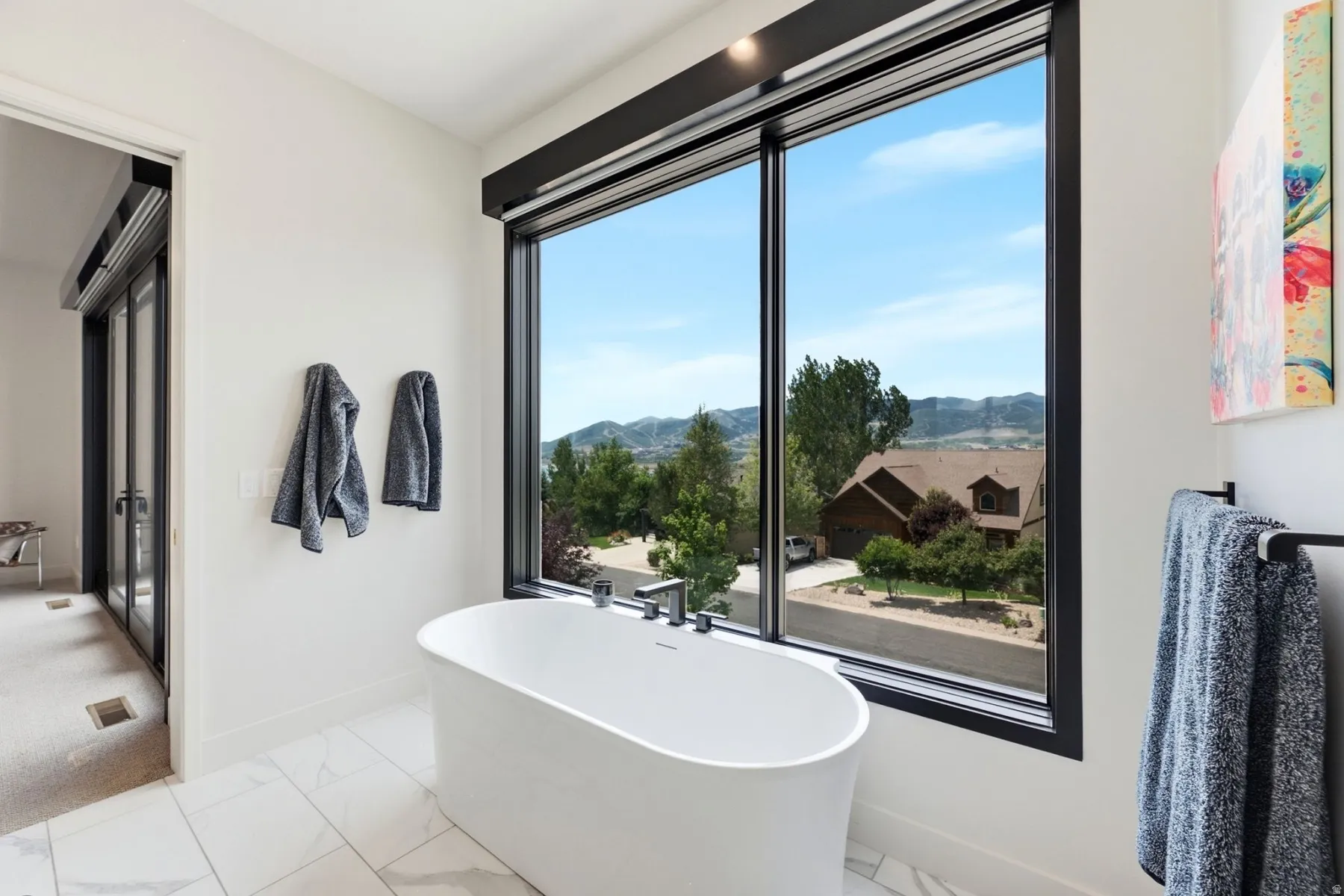 Freestanding soaking tub with a floor-mounted faucet, large picture window with black trim, and tile flooring