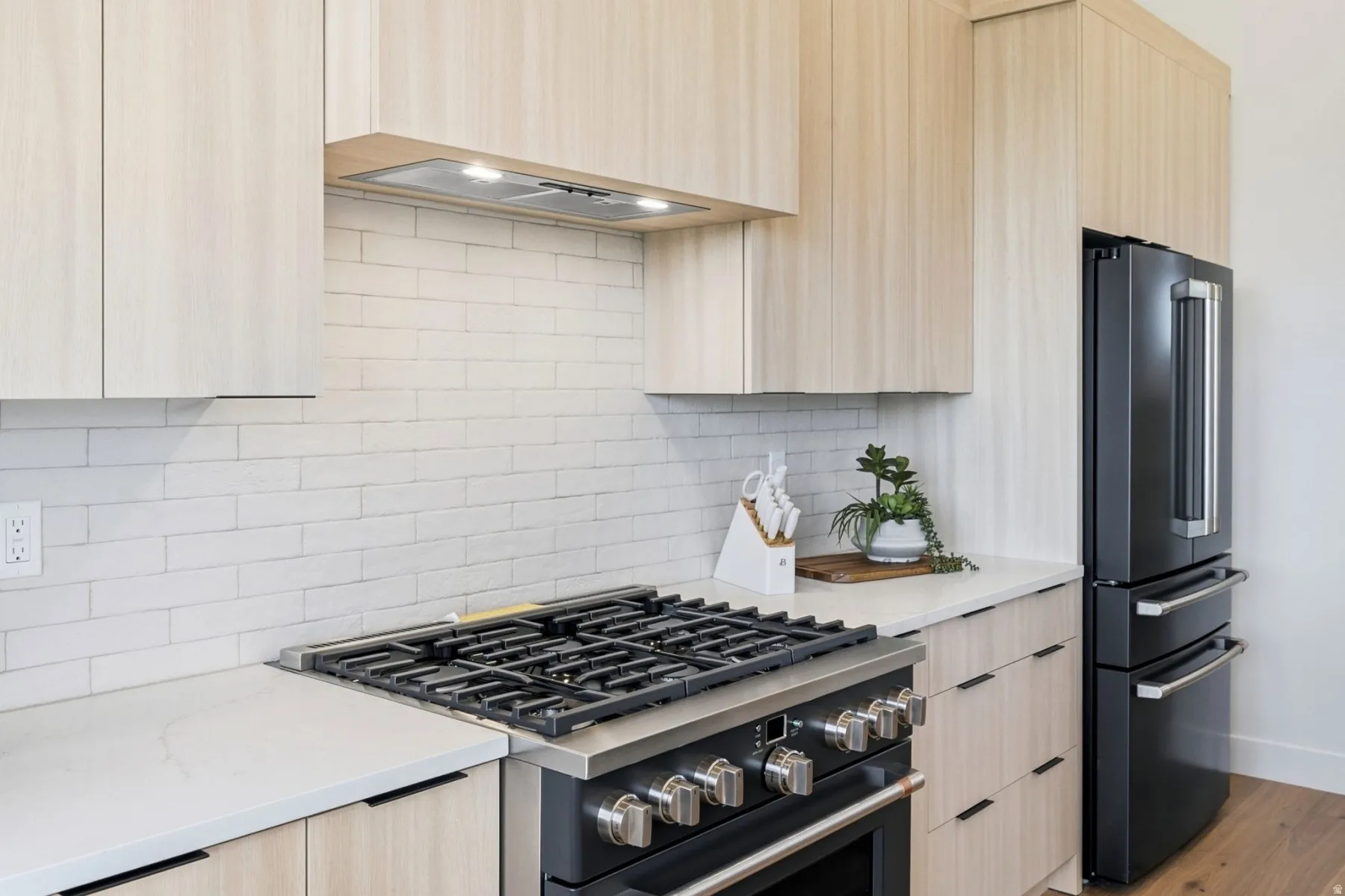 Modern kitchen featuring light wood-finish cabinetry, white subway tile backsplash, and light-toned countertops