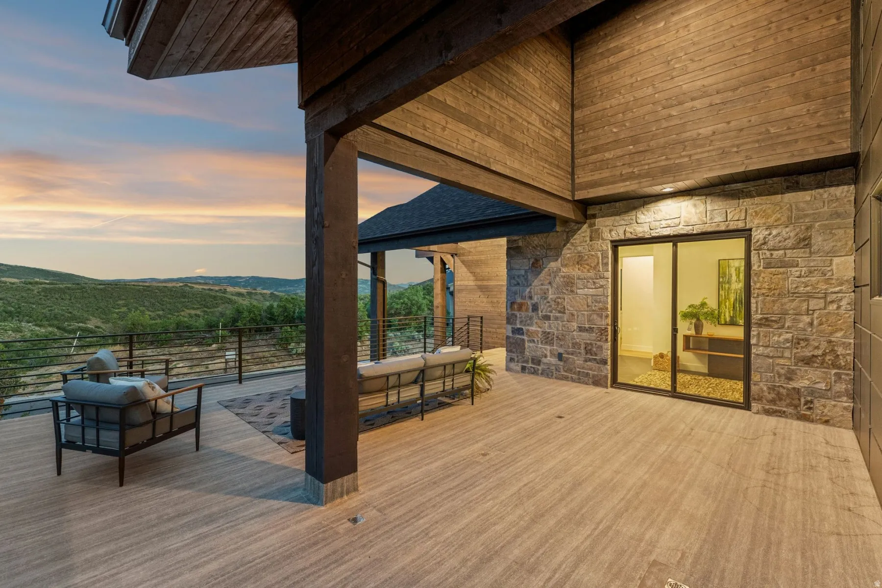 Expansive covered deck featuring wood-finish flooring, stone-clad exterior walls, and sliding glass doors