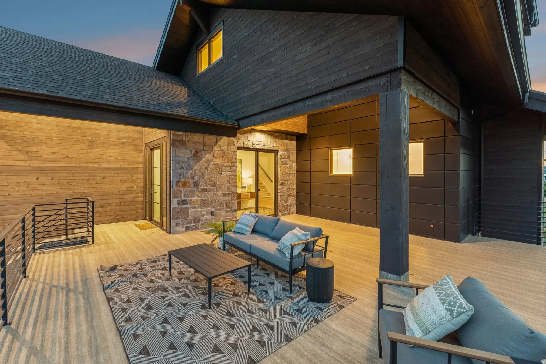 Expansive covered deck featuring wood-finish flooring, stone accent wall, and contemporary dark wood siding