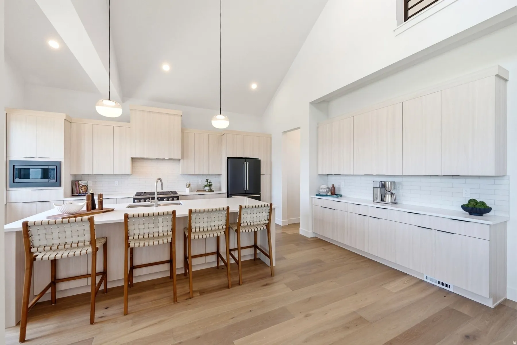 Kitchen featuring light wood-finish cabinetry, white subway tile backsplash, a large center island with counter seating, and wood-finish flooring