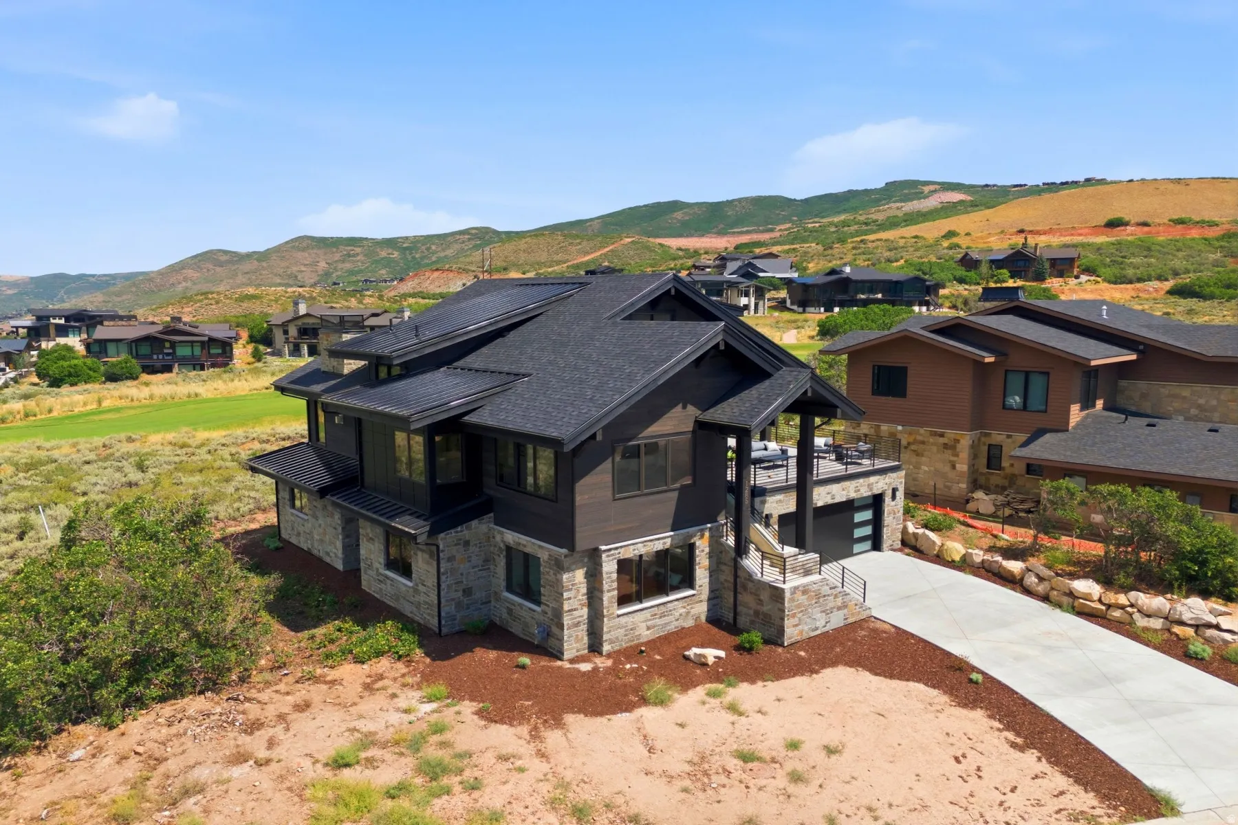 Modern multi-story residence featuring a stone and wood-panel exterior, dark shingle roof, integrated two-car garage with a contemporary door, and an upper-level balcony
