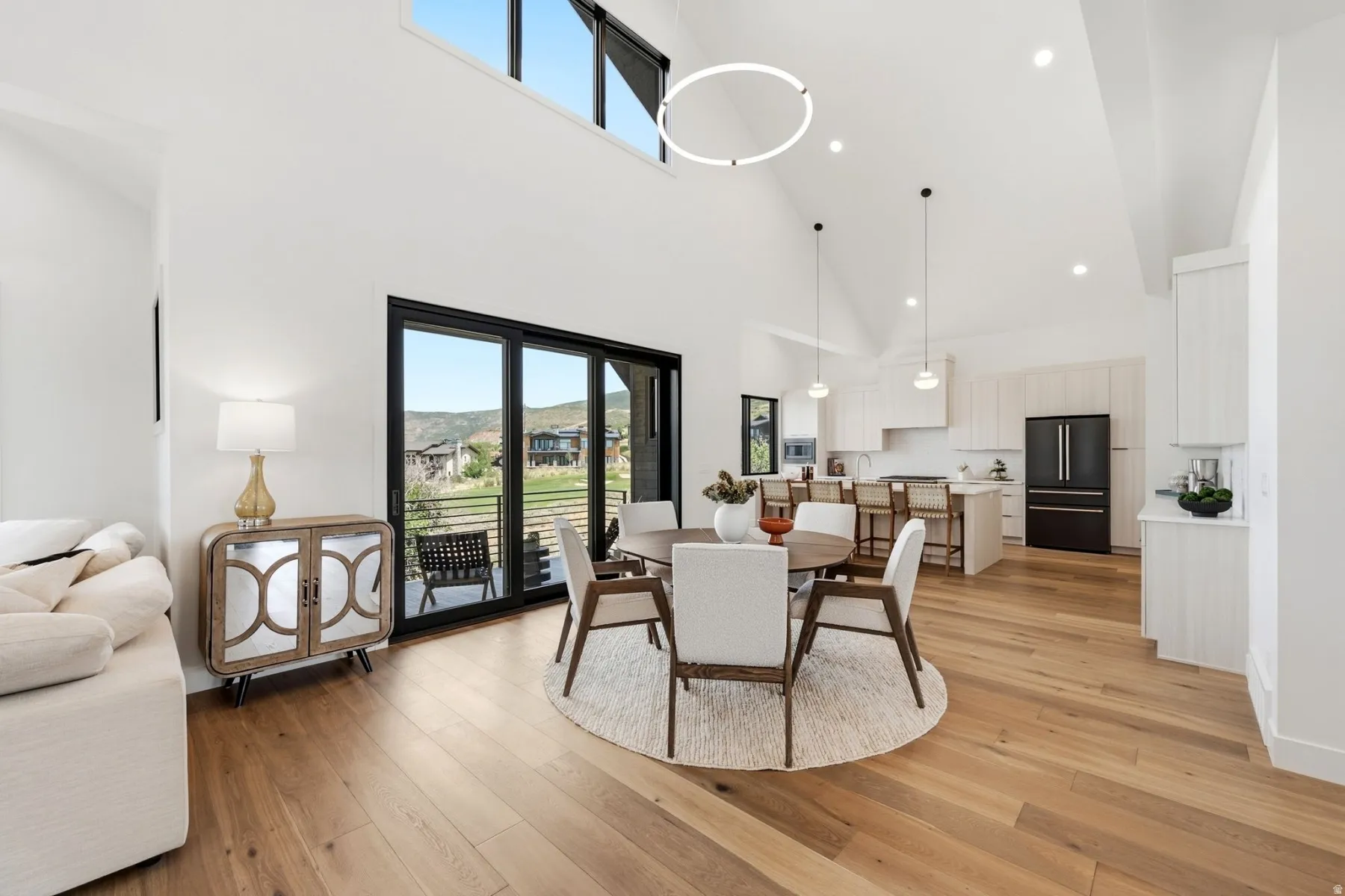 Vaulted ceilings, wood-finish flooring, a contemporary kitchen with white cabinetry, and sliding glass doors with direct outdoor access