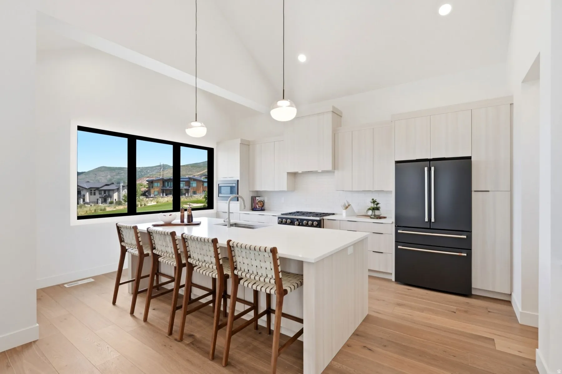 Vaulted ceiling with pendant lighting, kitchen island with seating, built-in stainless steel appliances, light wood-finish cabinetry, and wood-finish flooring