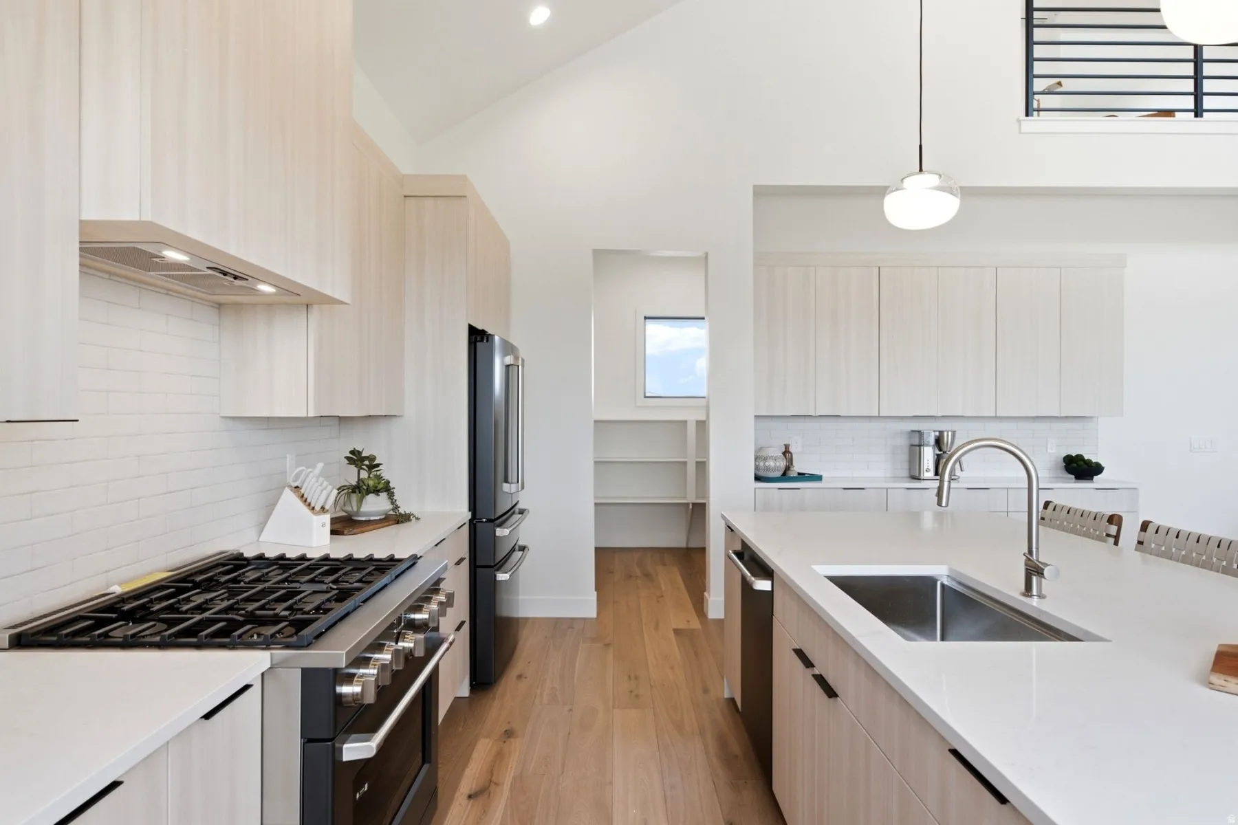 Vaulted ceilings with recessed lighting, wood-finish flooring, a stainless steel gas range with a matching hood, an integrated dishwasher, and a large kitchen island with an undermount sink