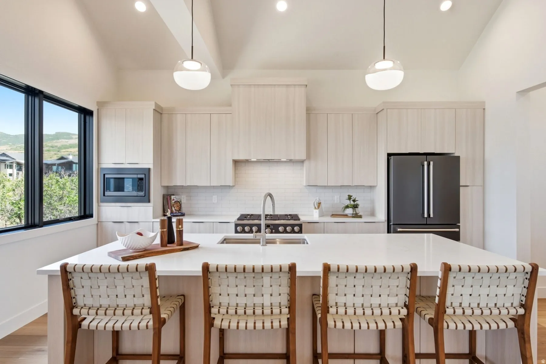 Kitchen featuring a large island with counter seating, light wood-finish cabinetry, a gas range, a built-in microwave, and a black French door refrigerator