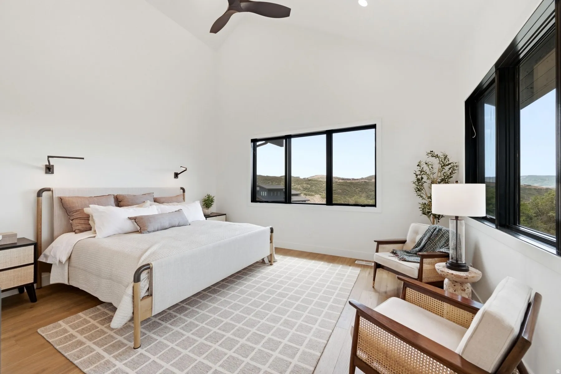 Vaulted ceiling with a ceiling fan, light wood-finish flooring, and multiple large windows with black frames