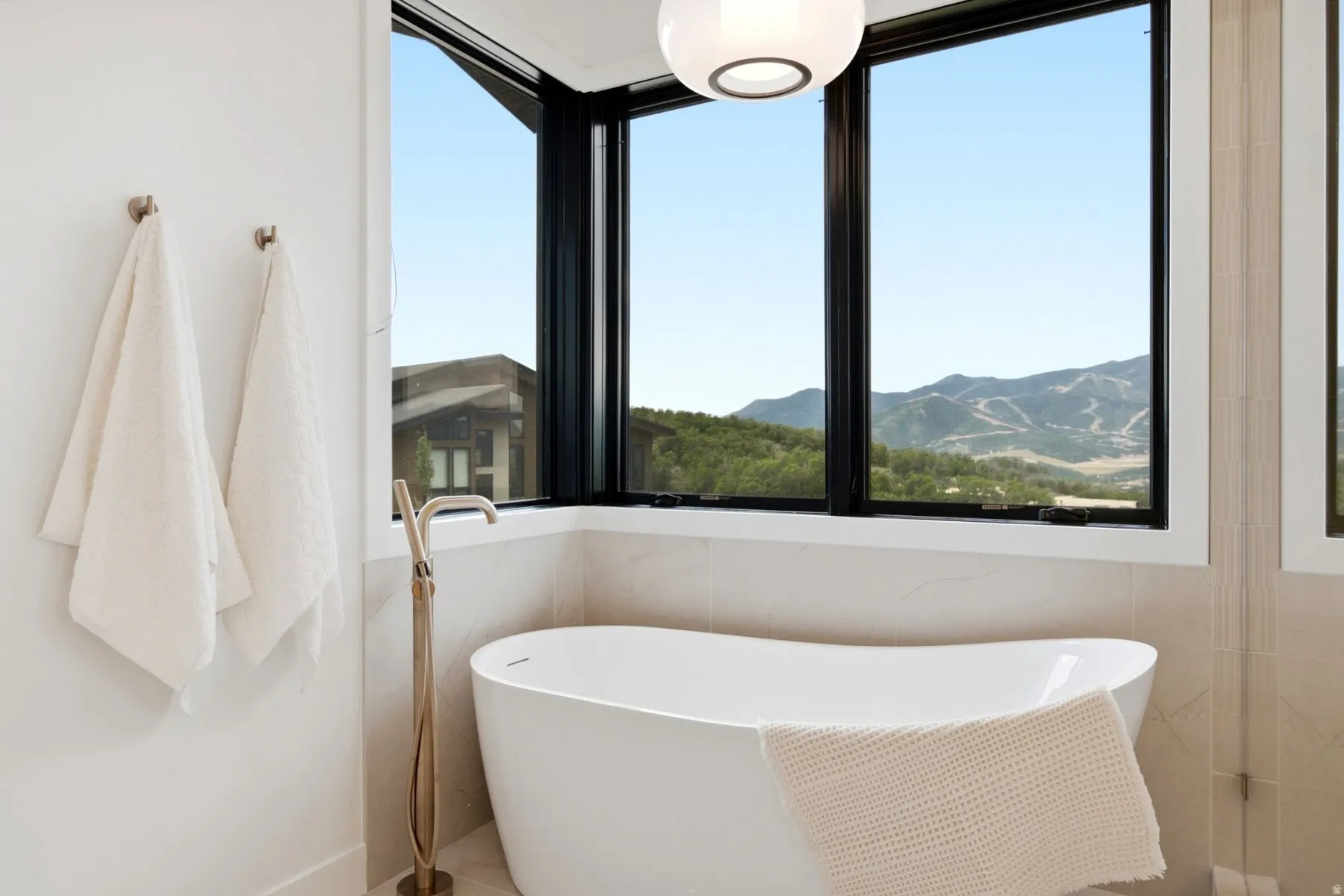 Corner window configuration with expansive mountain scenery, contemporary freestanding bathtub, and a floor-mounted faucet