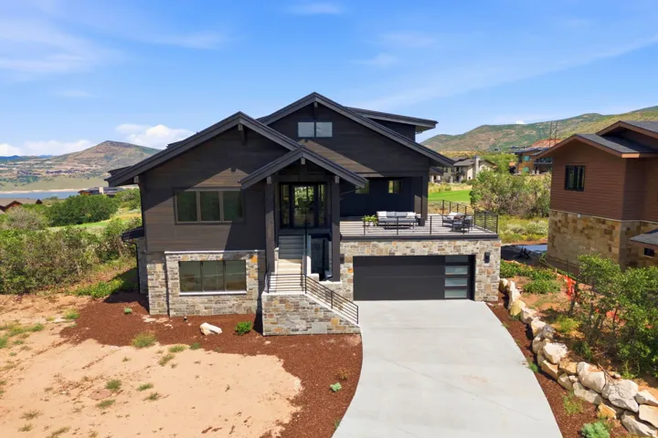 Modern exterior featuring dark siding, stone accents, a concrete driveway, an upper-level deck, and an attached garage with a contemporary door