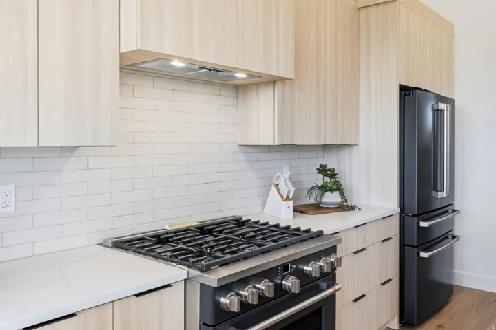 Modern kitchen featuring light wood-finish cabinetry, white subway tile backsplash, and light-toned countertops