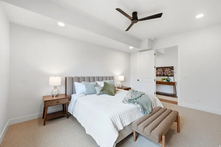 Recessed ceiling lighting, ceiling fan, white paneled door, light-toned carpet flooring, and a channel-tufted upholstered headboard