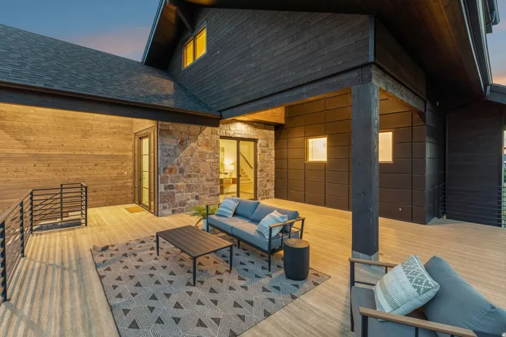 Expansive covered deck featuring wood-finish flooring, stone accent wall, and contemporary dark wood siding