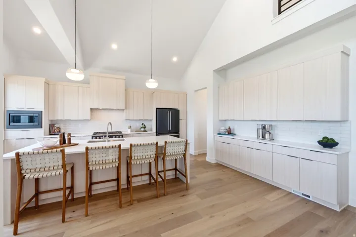 Kitchen featuring light wood-finish cabinetry, white subway tile backsplash, a large center island with counter seating, and wood-finish flooring