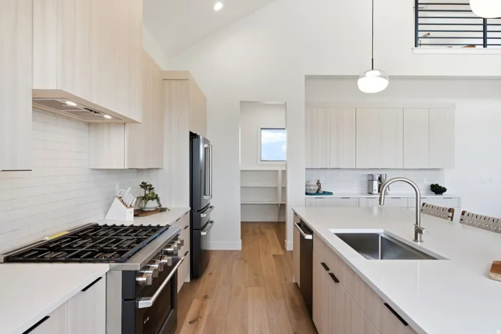 Vaulted ceilings with recessed lighting, wood-finish flooring, a stainless steel gas range with a matching hood, an integrated dishwasher, and a large kitchen island with an undermount sink
