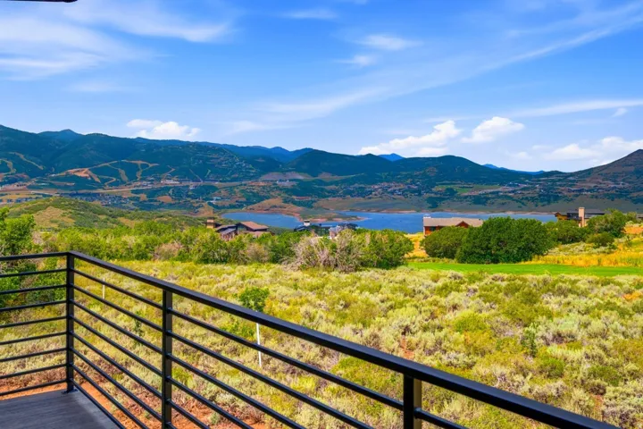 Exterior balcony with a black horizontal-bar railing, showcasing expansive mountain and lake scenery, and varied natural landscaping