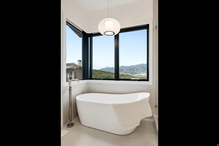Freestanding soaking tub with floor-mounted brushed nickel faucet, large corner windows with black frames, and a modern spherical pendant light