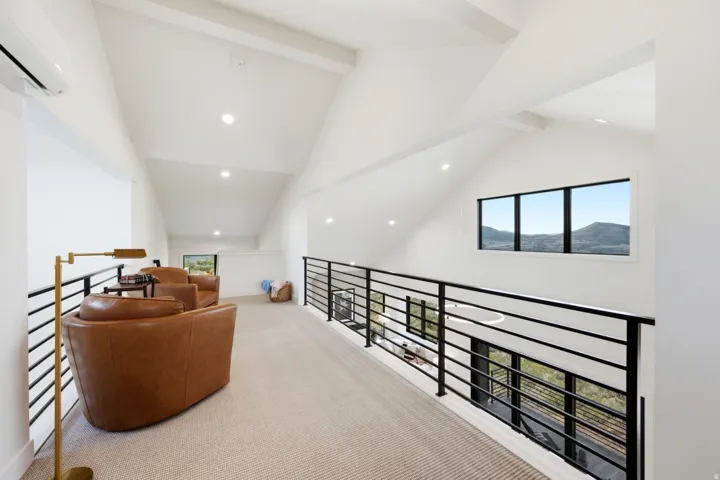 Vaulted ceilings with exposed beams, recessed lighting, and a black metal railing system