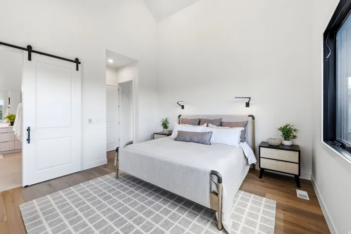 Vaulted ceiling, wood-finish flooring, black-framed window, barn door entry, and wall-mounted sconces