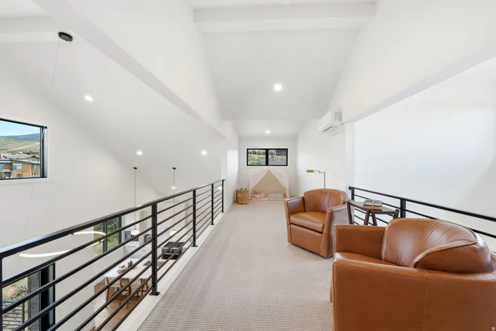 Upper-level loft with sloped ceilings, black metal railings, recessed lighting, and a ductless mini-split system