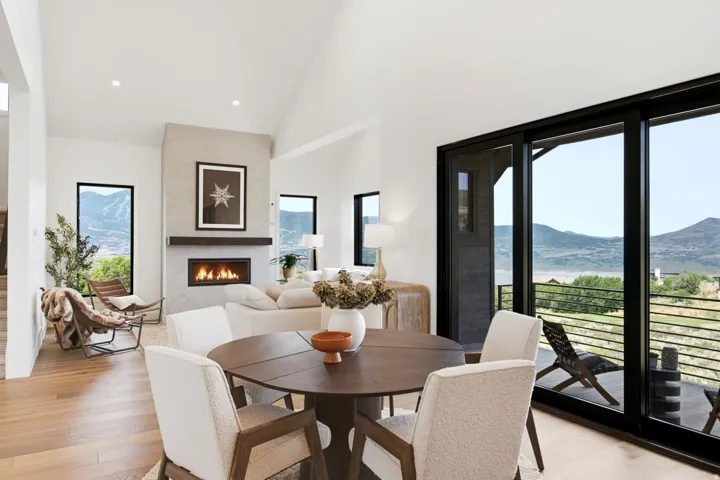 Vaulted ceilings, wood-finish flooring, a contemporary fireplace, and black-framed sliding glass doors opening to an outdoor balcony