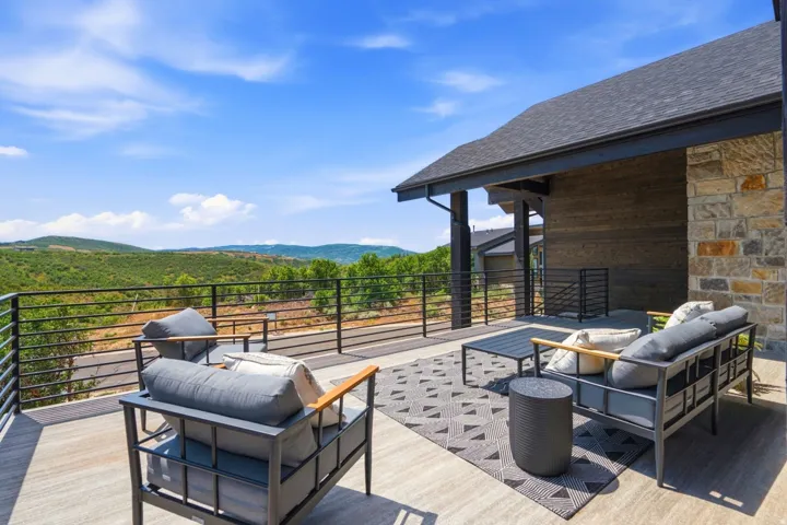 Expansive outdoor patio with metal railings, a stone and wood-paneled exterior, and an asphalt shingle roof
