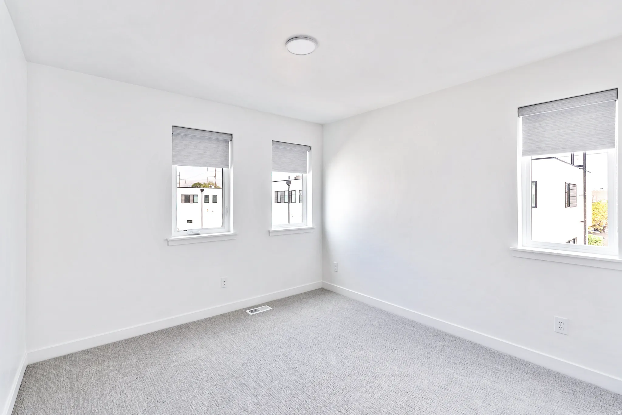 Light gray carpeting and white walls with three windows featuring blinds