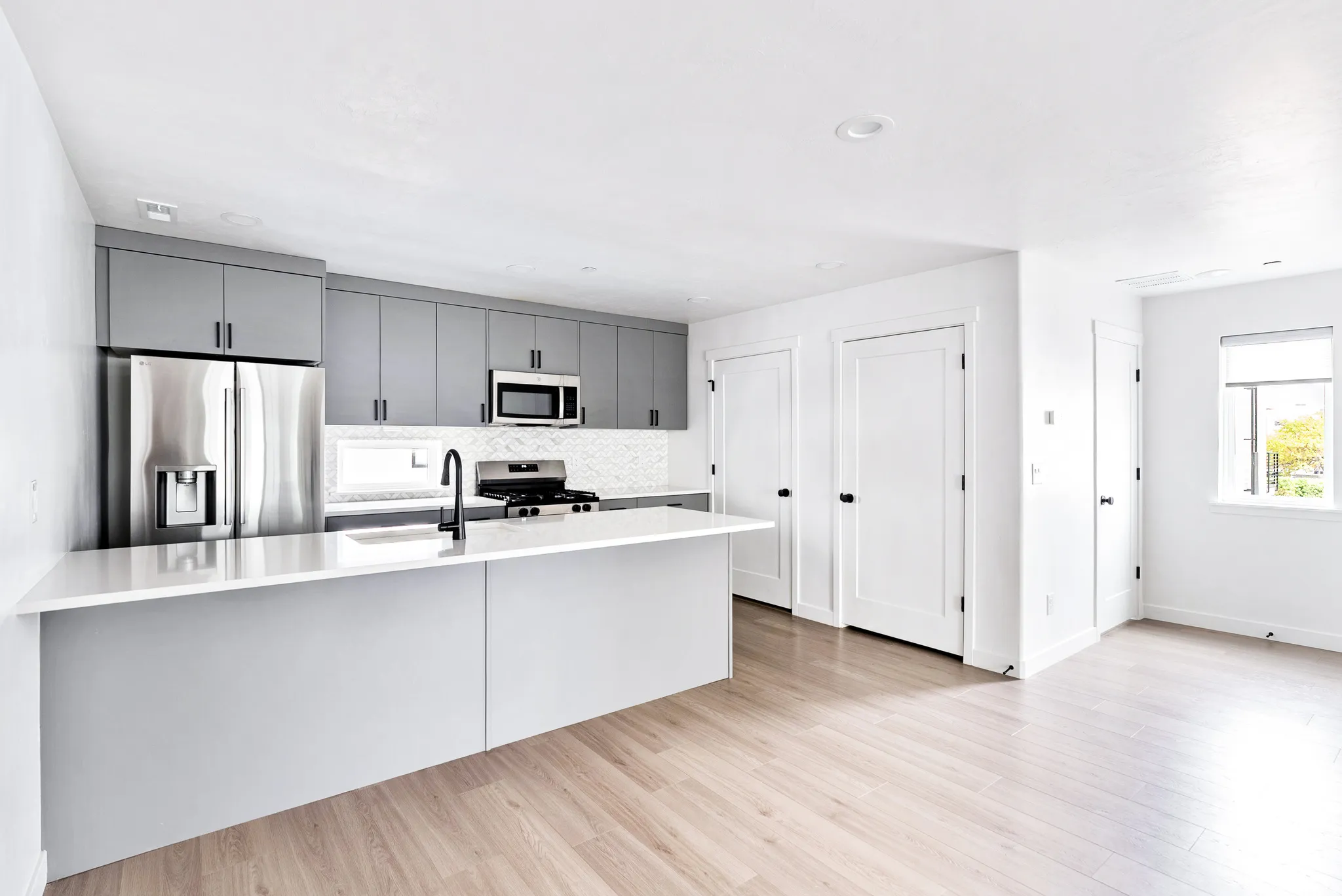 Kitchen featuring light gray cabinetry, stainless steel appliances, white countertops, and a white tile backsplash