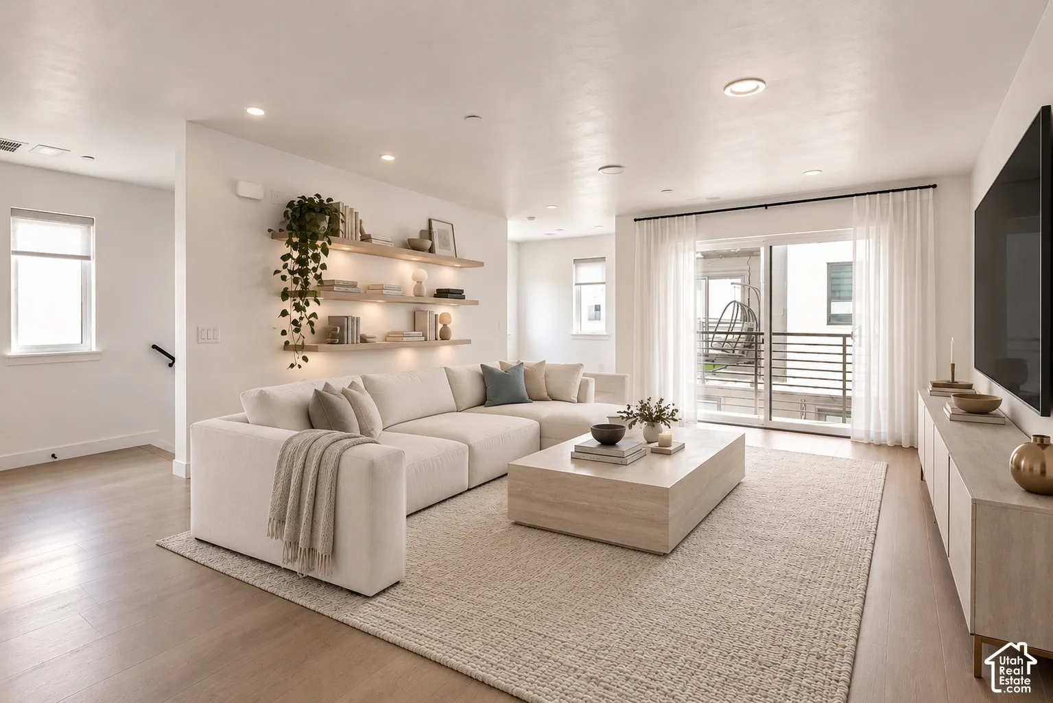 Living area featuring light-toned wood-finish flooring, recessed lighting, and wall-mounted floating shelves with integrated accent lighting