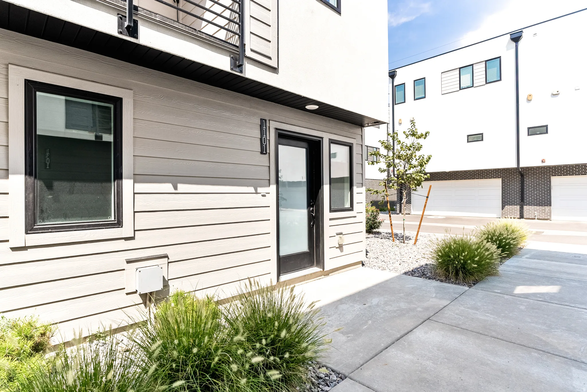 Modern exterior siding, large framed windows, black trim accents, concrete pathway, and landscaped rock and shrubbery