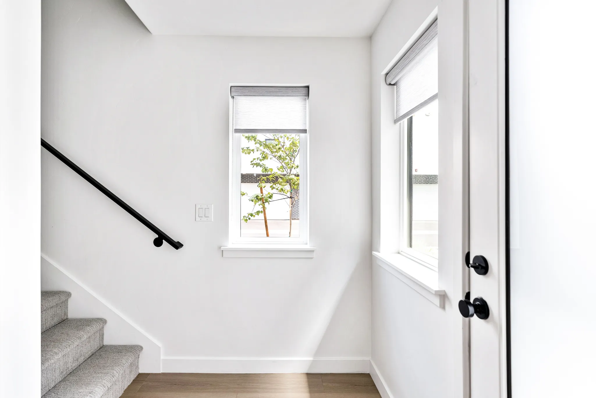 Hardwood-style flooring, white walls, carpeted staircase with a black handrail, and multiple windows