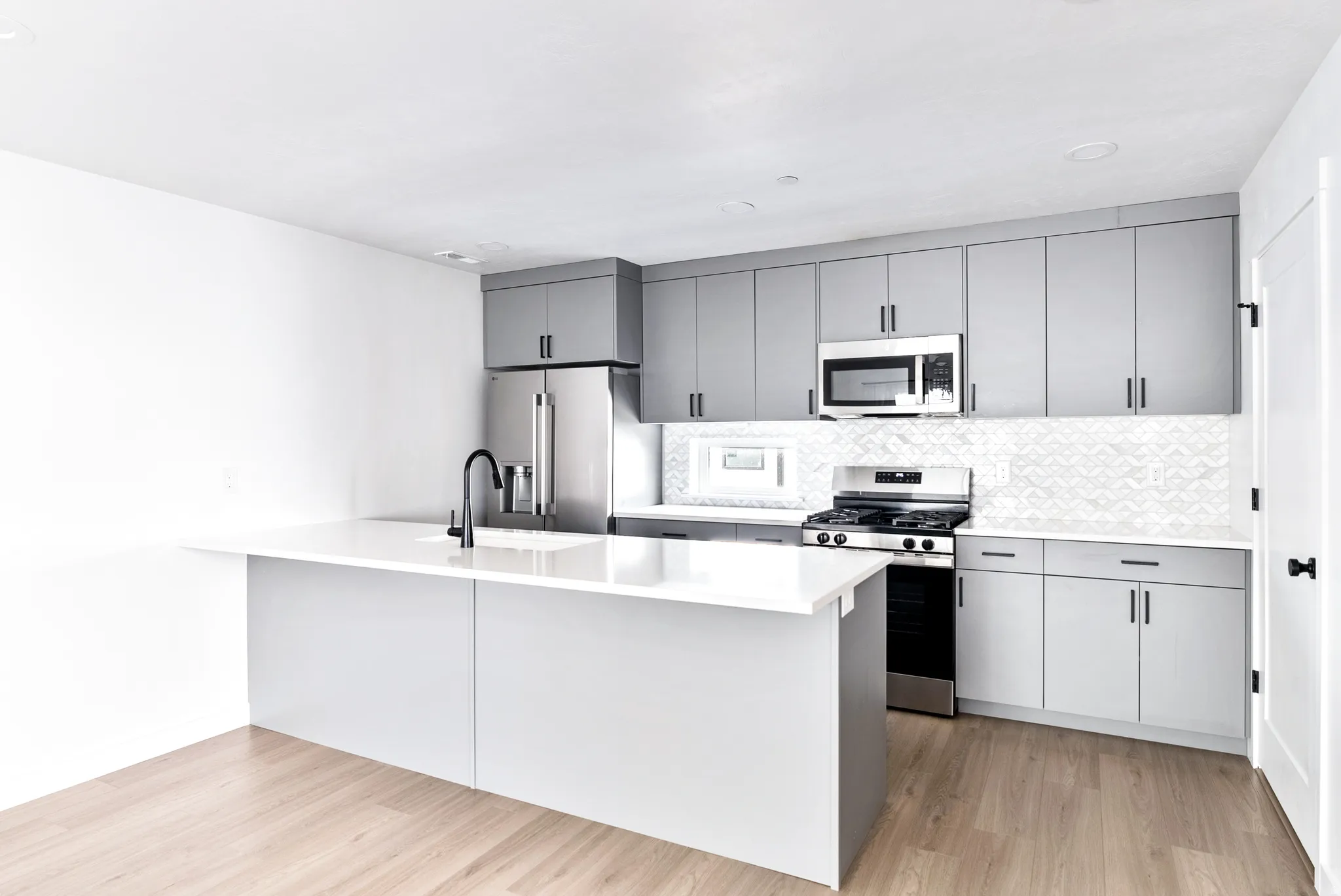 Kitchen featuring wood-finish flooring, white countertops, gray cabinetry, stainless steel appliances, and a tiled backsplash