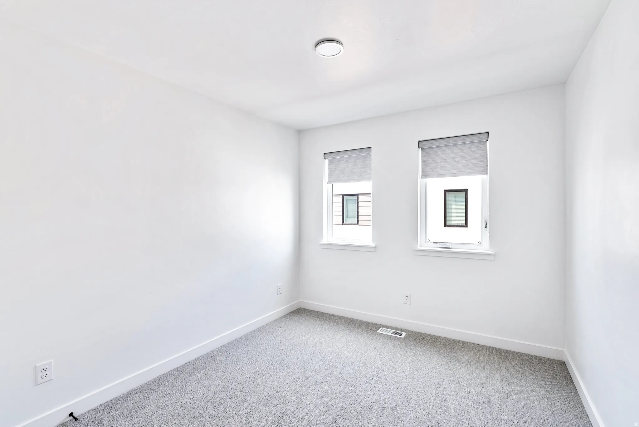 White walls, recessed lighting, two windows with roller shades, and light-toned carpeting